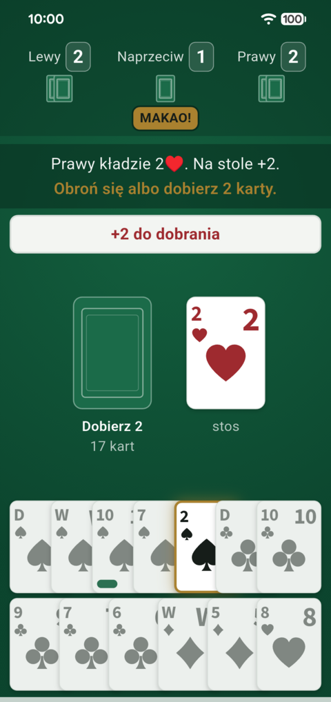 Stół Makao z karą: żeton „+2 do dobrania”, nad stołem „Obroń się albo dobierz 2 karty”, pod talią „Dobierz 2”, a w ręce podświetlona jedyna karta, którą wolno się obronić — dwójka pik